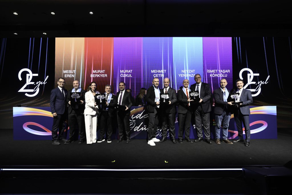 A line of male employees in suits holding service awards on a stage.