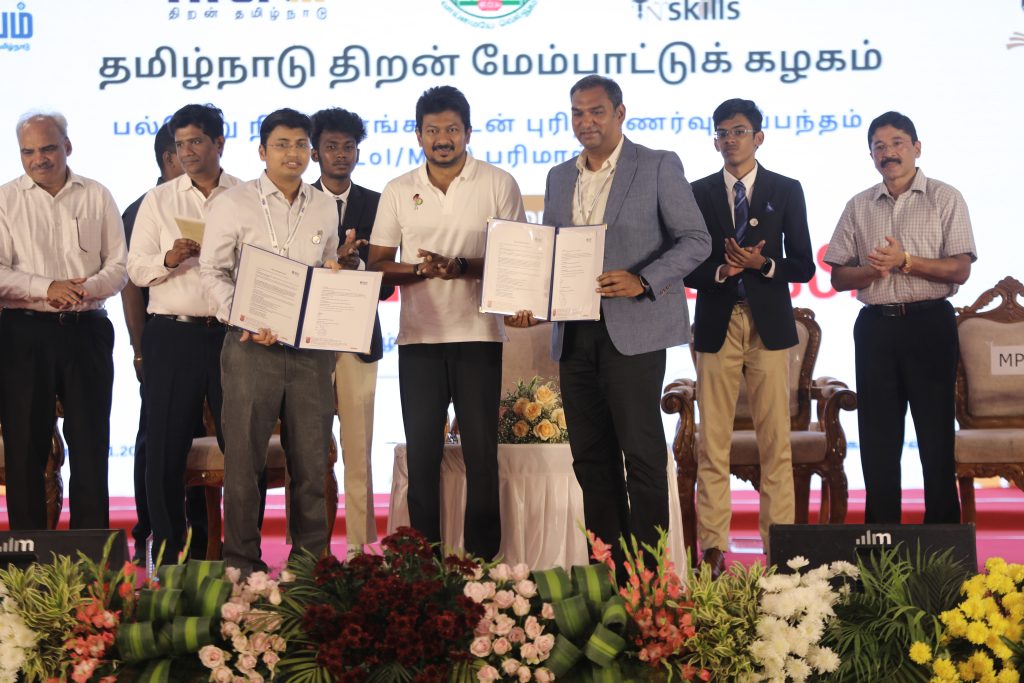 Officials holding signed agreement documents on stage at the TN Skills 2025 ceremony.