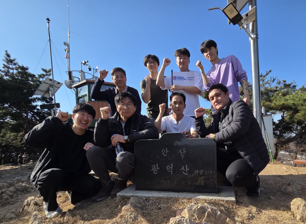 A group of employees hiking and posing by a mountain marker during a charity event.