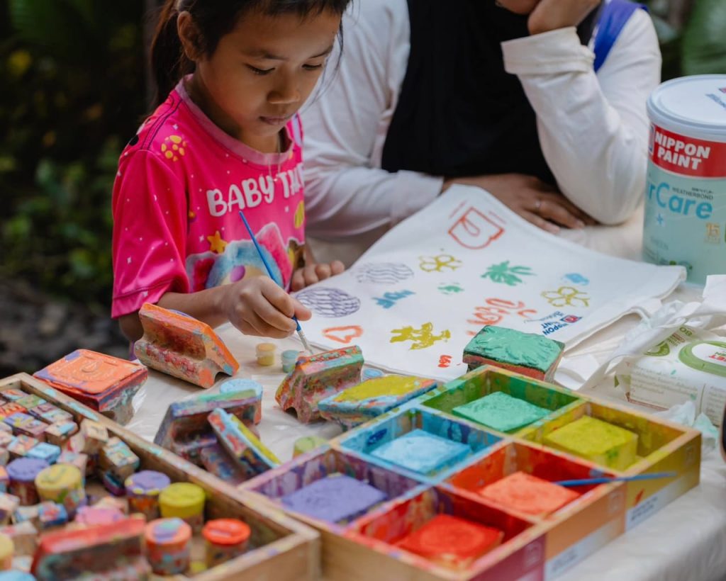A young girl painting designs on a canvas bag at an outdoor workshop.