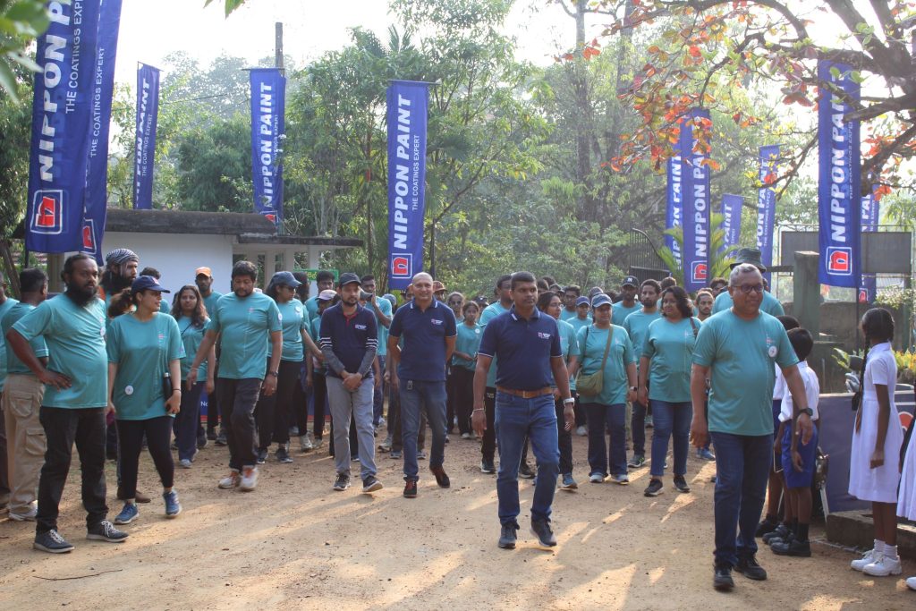 A large group of volunteers in matching teal shirts walking together outdoors.
