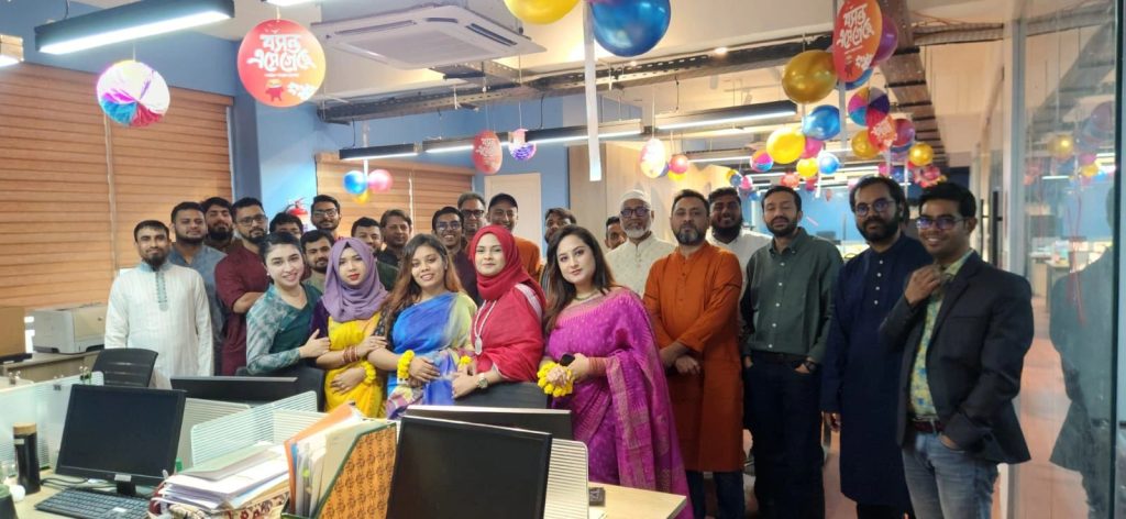 A large group of employees dressed in colourful traditional attire posing in a decorated office space.