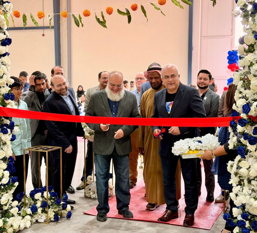 Several men smiling as they cut a red ribbon during a facility opening ceremony.