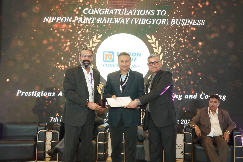 Three men on stage holding a trophy and a certificate for the Nippon Paint Railway Business award.