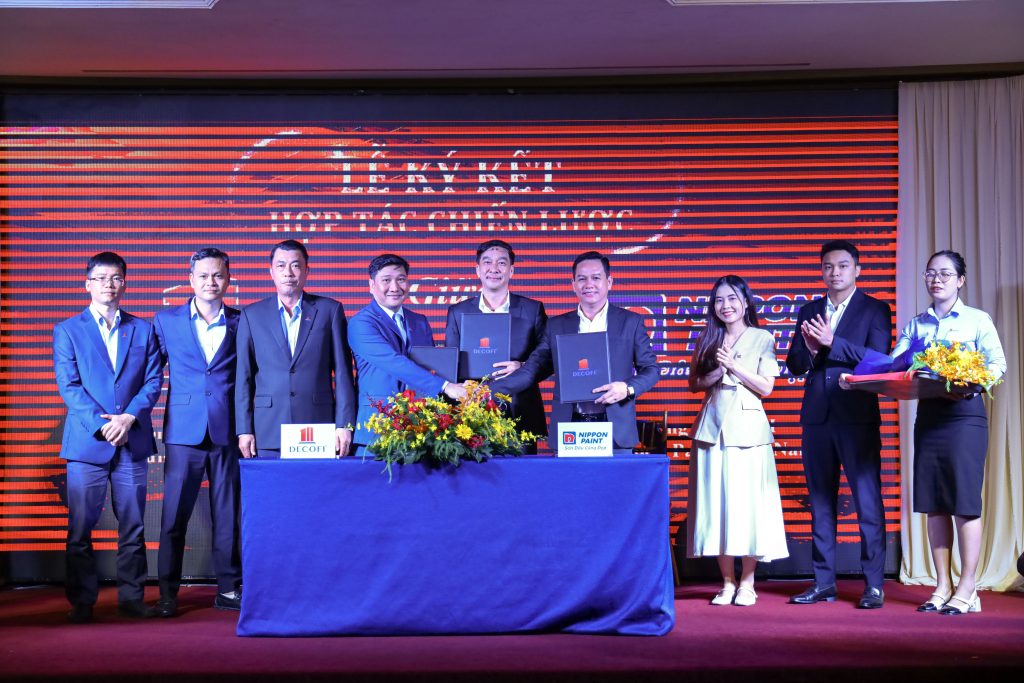 Representatives from Nippon Paint Vietnam and DECOFI shaking hands and exchanging signed agreements on stage.