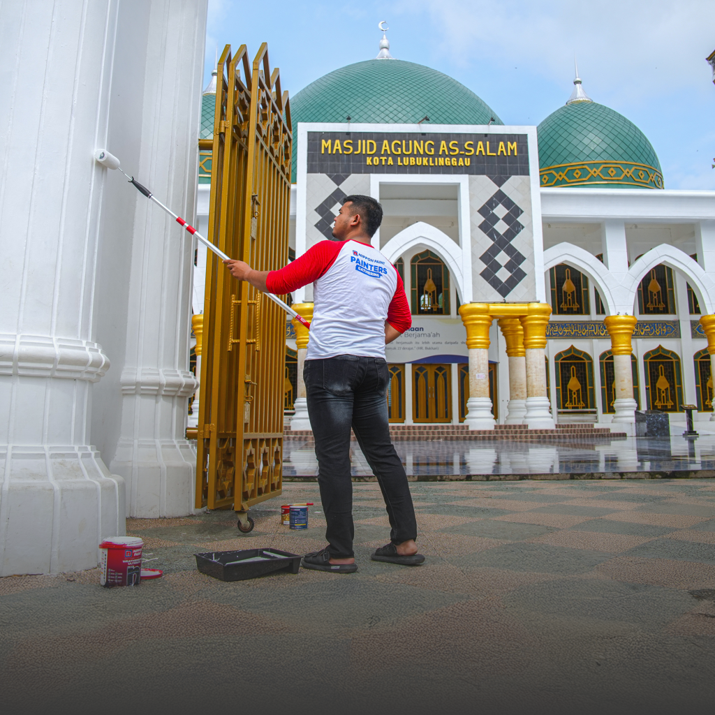 A man using a roller to paint the exterior pillars of Masjid Agung As-Salam. 