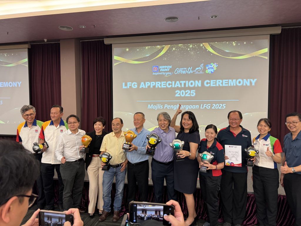 A group of Nippon Paint Malaysia leaders and employees posing happily on stage with their robot-shaped LFG trophies.