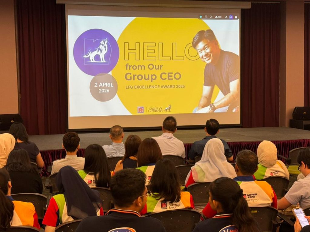 A group of employees sitting in a hall, watching the "Hello from Our Group CEO" presentation on a large projection screen.