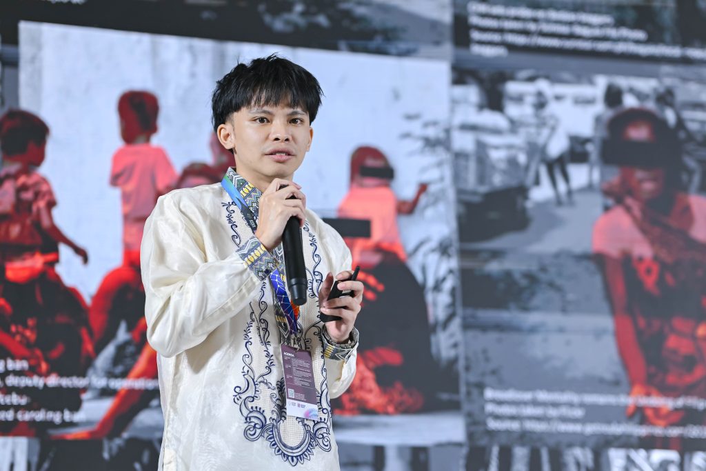 Ejhey Durias, wearing a traditional Barong, speaking passionately into a microphone during his on-stage presentation.  