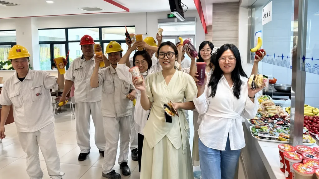 Smiling employees holding up fresh drinks and fruit in a cafeteria setting.